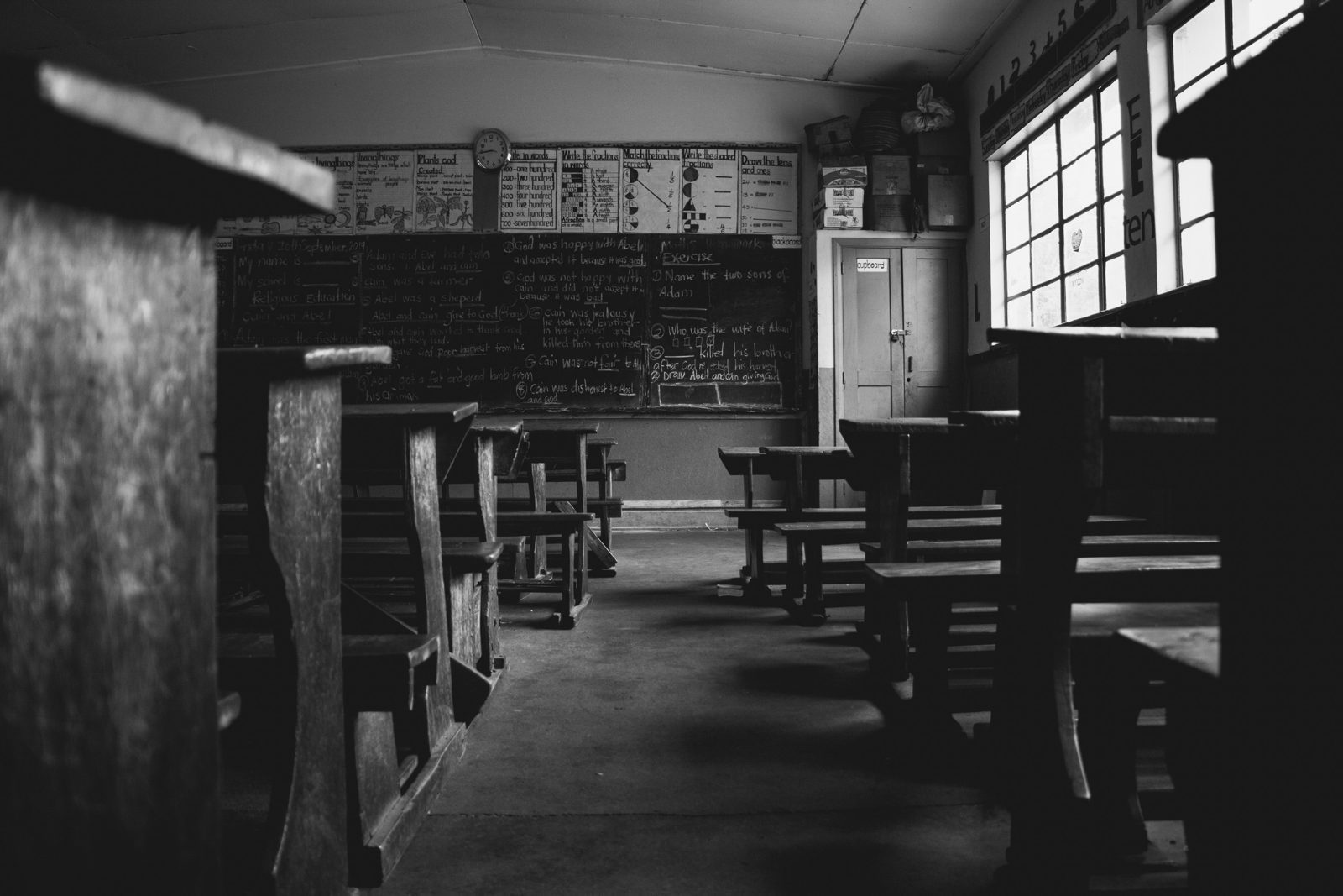 An empty classroom with wooden benches and a chalkboard